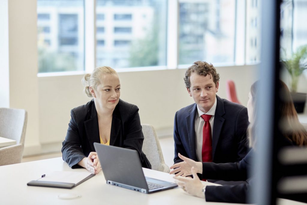 Three people having a meeting in an office looking at a laptop