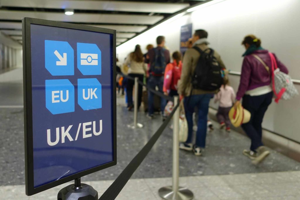 A UK/EU sign at the arrivals section of an airport with people queueing