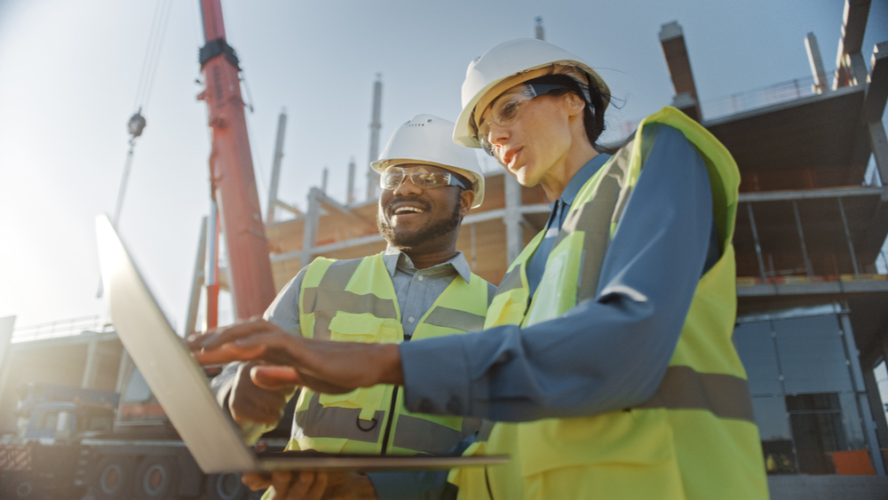 Two people in hard hats in discussion with a laptop on a development site